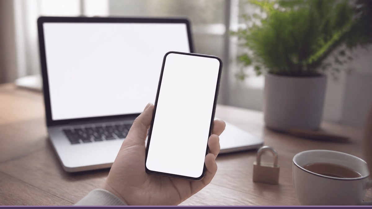Hand holding a smartphone in front of a laptop with a padlock on the desk, checking website security and mobile view
