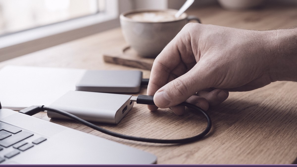 Hand plugging a portable drive into a laptop on a wooden desk to restore a WordPress backup after a failed update